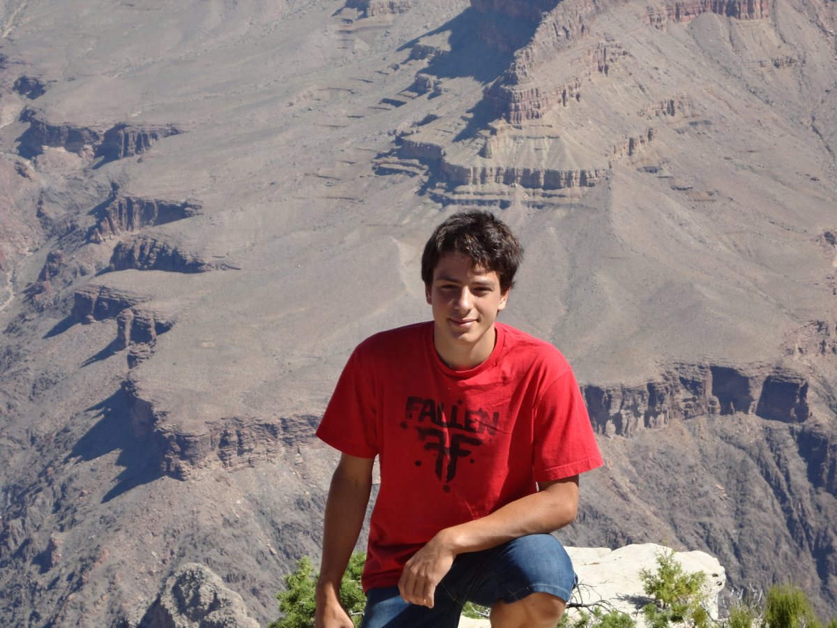 Marco Gallo seduto su una roccia con un grande canyon sullo sfondo, maglietta rossa, sguardo verso l'obiettivo.